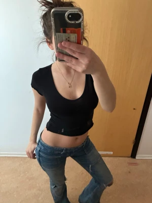 Svart croppad topp med djup ringning - En svart, croppad topp med djup v-ringning och korta ärmar. T-shirten har en tight passform och är tillverkad i ett stretchigt material som sitter snyggt på kroppen. Perfekt för en trendig och avslappnad look.