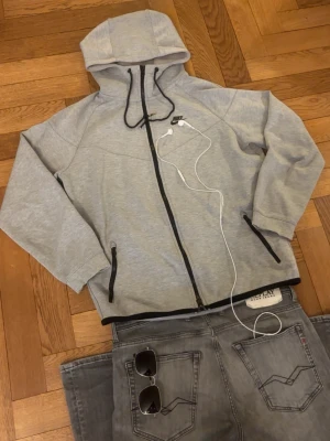 Grå zip hoodie från Nike - Grym kvalité, inga defekter. Storlek är M, passformen sitter bra. Men Kolla måtten så de passar:)  Mått -|-  Axelmått: 55 cm  Längd: 64 cm  Bröst: 57 cm  Arm: 52 cm  Leverans sker dagen efter, men har du nån fråga är det bara att skriva :)