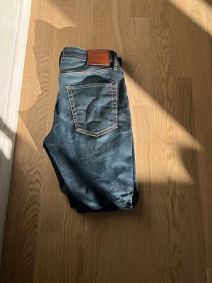 Blå jeans med läderpatch - Snygga blå jeans med klassisk femficksdesign och kontrastsömmar. Jeansen har en brun läderpatch bak i midjan och raka ben. Perfekta för en avslappnad och trendig look.