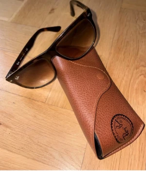 Brun läderhandväska med mönster - Cool brun handväska i läder med snyggt mönster på framsidan. Väskan har en klassisk rektangulär form och ett praktiskt handtag upptill. Perfekt för dig som gillar vintage vibes och detaljer.