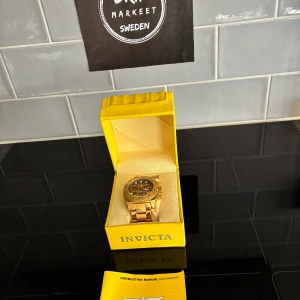 Guldig Invicta klocka  - Säljer en snygg och maffig guldig klocka från Invicta med metallarmband och svart urtavla. Klockan har flera små urtavlor och tydliga siffror på ringen. Kommer i original gul box med manual. Perfekt för dig som gillar statement-accessoarer.