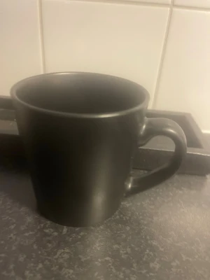 Svart matt mugg i keramik - En stilren svart mugg med matt finish och klassisk form. Tillverkad i keramik och har ett rejält handtag som gör den enkel att hålla i. Perfekt för kaffe, te eller varm choklad.