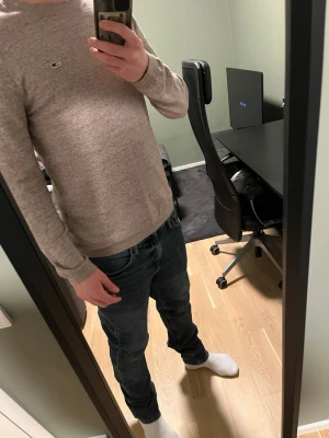 Beige stickad tröja  - Snygg beige stickad tröja från Tommy Jeans med rund halsringning och diskret logga på bröstet. Tröjan har långa ärmar och är tillverkad i mjukt material som passar perfekt till lager på lager. Enkel och stilren design.