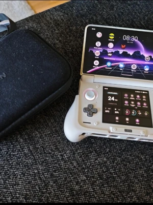 AYN Odin 2 Pro bärbar spelkonsol - Säljer en AYN Odin 2 Pro, en bärbar spelkonsol i ljusgrått med dubbla skärmar och klassiska spelknappar. Konsolen har en modern design med färgglada knappar och styrspakar. Perfekt för retrospel och emulering, med Android-gränssnitt och tillhörande skyddsväska.