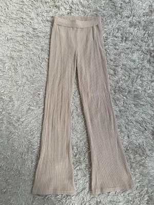 Beigea utsvängda byxor - Säljer ett par beige ribbade byxor med utsvängda ben och medelhög midja. De är stretchiga och har en bred resår i midjan för extra komfort. 