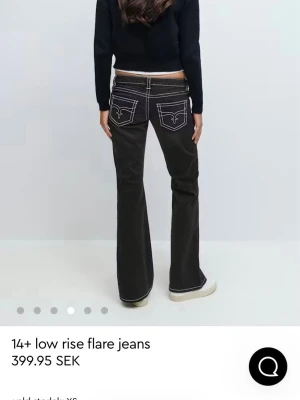 Svarta low rise flare jeans - Snygga svarta jeans med låg midja och utsvängda ben. Jeansen har vita kontrastsömmar och dekorativa bakfickor med broderad detalj. Perfekta för en trendig och avslappnad look. Materialet är klassisk denim. Säljer dessa för att dem inte kommer till andvändning 