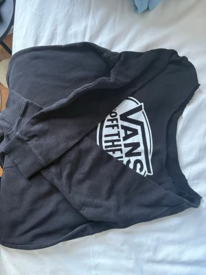 Off shoulder vans tjocktröja - Svart hoodie från Vans med klassiskt vitt 'Off The Wall'-tryck på bröstet. Mjuk bomullskänsla och ribbade muddar vid ärmslut och midja. Perfekt för en avslappnad streetwear-look.