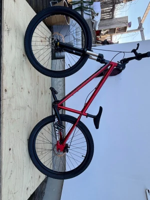 Röd trialcykel med svart sadel - Säljer en röd trialcykel med svart sadel och svarta handtag. Cykeln har robust ram, grova däck och skivbromsar. Perfekt för dig som gillar att köra trial eller vill ha en cool cykel för tricks. Märket syns på bakgaffeln: trial-bikes.com.