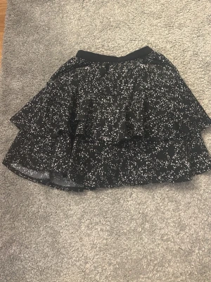 Svart volangkjol med vitt mönster från pompdelux - Säljer en svart kortkjol med volang från pompdelux med vita småprickiga detaljer.