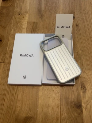 RIMOWA mobilskal iPhone 17 Pro Max - Snyggt mobilskal från RIMOWA i silverfärgad aluminium med klassisk räfflad design och grå kanter. Skalets insida är ljusgrå och har RIMOWA-loggan tryckt. Kommer i originalförpackning med tillhörande dokumentation.