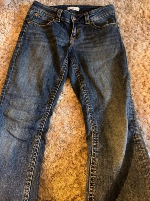 Blå bootcut jeans från Gina Tricot  - Säljer ett par klassiska blå bootcut jeans från Gina Tricot med fem fickor och snygga slitningar. Jeansen har en normal midja och är tillverkade i denim med en autentisk tvätt. Perfekta för dig som gillar en avslappnad och tidlös look.