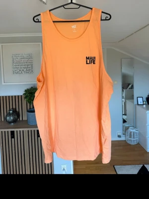 Persikofärgad linnetopp från 157 - Säljer en persikofärgad ärmlös linnetopp från 157 med trycket 'MAUI LIFE' på bröstet. Toppen är tillverkad i 100% bomull och har en avslappnad passform, perfekt för varma dagar.