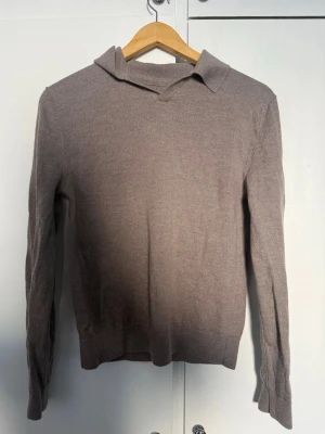 Beige merinotröja från These Glory Days - Snygg beige stickad tröja från These Glory Days i mjuk merinoull. Tröjan har lång ärm, krage och ribbade muddar. Perfekt för lager-på-lager och enkel att matcha med jeans eller chinos.