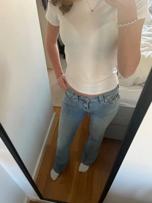 Ljusblå bootcut jeans från True Religion - Säljer ett par ljusblå bootcut jeans från True Religion med mid midja och klassiska femficksdetaljer. Jeansen har snygga bakfickor med knapp och en liten True Religion logga på baksidan. De är bra skick men har små slitningar längst ned. 