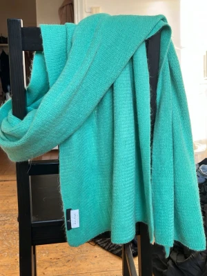 Turkos halsduk från Åhléns - Snygg turkos halsduk från Åhléns i mjukt stickat material. Halsduken är rektangulär och har en enkel, stilren design utan fransar. Perfekt att svepa runt halsen för extra värme och färg till din outfit.