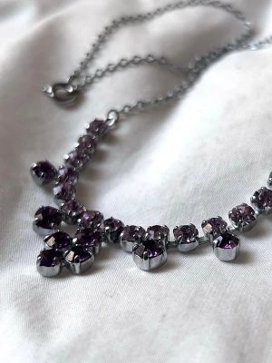 Silverfärgat halsband med lila stenar - Ett snyggt halsband med gnistrande lila och ljuslila stenar i olika storlekar. Stenarna är runda och sitter tätt längs kedjan. 