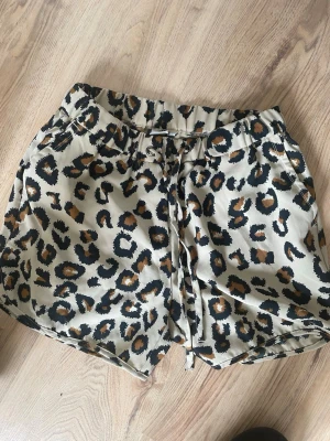 Leopardmönstrade shorts med snörning - Snygga shorts med leopardmönster i beige, svart och bruna toner. De har en avslappnad passform och snörning i midjan för extra komfort. Perfekta för varma dagar när du vill sticka ut lite extra.med fickor på sidorna 