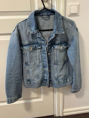Klassisk blå jeansjacka - Snygg blå jeansjacka i klassisk modell med raka sömmar och två bröstfickor med knappar. Jackan har en avslappnad passform, knappstängning framtill och justerbara knappar i midjan. 