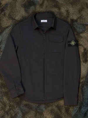 Svart overshirt från Stone Island - Snygg svart overshirt från Stone Island med dragkedja framtill, klassisk krage och bröstficka med lock. Ikonisk Stone Island-patch på vänster ärm. Tillverkad i ett slitstarkt material som ger en clean och modern look.