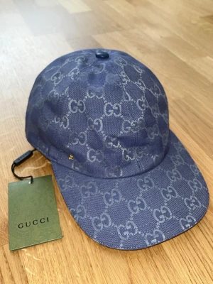 Blå keps från Guc ci med GG-mönster - Snygg blå keps från Guc ci med det klassiska GG-monogrammet över hela kepsen. Tillverkad i ett tåligt tygmaterial och har en böjd skärm. Perfekt för dig som vill ha en exklusiv och trendig accessoar till din outfit.