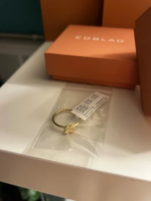 Guldfärgad ring med fyrklöver - Snygg och stilren guldfärgad ring med en liten fyrklöverdetalj framtill. Ringen har en tunn och enkel design som gör den lätt att matcha med andra smycken. Perfekt för dig som gillar minimalistiska accessoarer med en söt twist. Storlek s (16,8 mm)