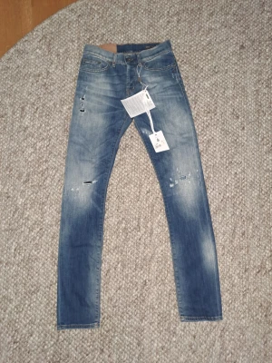 Dondup Jeans - Snygga blå slim fit jeans med slitningar och ljusa tvättade partier. Jeansen har klassisk femficksdesign, hällor för bälte och dragkedjegylf. Materialet är denim med stretch för extra komfort. Perfekta för en trendig och avslappnad look.