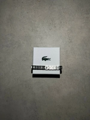 Silverfärgat armband från Lacoste - Snyggt armband i silverfärgad metall från Lacoste. Armbandet har en stilren och modern design med rektangulära länkar och diskret Lacoste-logga. Perfekt accessoar för dig som gillar minimalistisk och sportig stil.