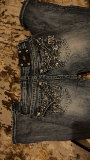 Y2K jeans - Snygga blå jeans med slitningar och massor av strass och nitar på både bakfickor och framfickor. Jeansen har en tvättad look och dekorativa sömmar, perfekt för dig som gillar att sticka ut med din stil. Pris kan diskuteras vid snabbt köp!