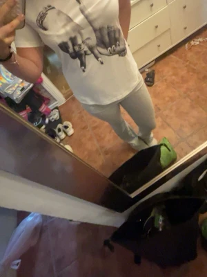 Vit t-shirt med tryck av händer - Säljer en vit t-shirt med ett stort svartvitt tryck av två händer med smycken och nagellack på framsidan. T-shirten har rund hals och korta ärmar. Perfekt för dig som vill ha en cool och unik look.