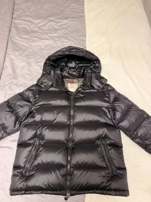 Svart dunjacka från Moncler - Säljer en snygg och varm Moncler dunjacka i svart. Jackan är i mycket fint skick och har använts varsamt. Den är både stilren och bekväm, perfekt för höst och vinter.  Skick:  *  bra skick * Dragkedjor och knappar fungerar som de ska * Inga hål eller större skador * Ren och redo att användas  Detaljer:  * Färg: Svart * Avtagbar huva * Två fickor med dragkedja * Moncler-logga på ärmen * Varm och lätt dunfyllning  Säljs eftersom den inte används längre.