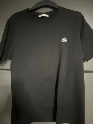 Svart Moncler t-shirt med logga - Snygg svart t-shirt från Moncler med klassisk rund hals och diskret Moncler-logga på bröstet. Enkel och stilren design som passar till det mesta. Tillverkad i mjuk bomull för skön känsla hela dagen.