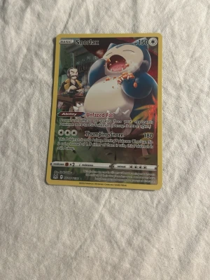 Snorlax Pokémonkort - Säljer ett Snorlax Pokémonkort med guldkant och färgglad illustration. Kortet har HP 150 och visar Snorlax som äter mat. Text och effekter på engelska. Perfekt för samlare eller Pokémonfans.