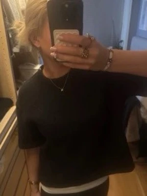 Svart croppad stickad topp - En svart, croppad stickad topp med korta ärmar och rund hals. Toppen har en loose passform och är perfekt för dig som gillar en enkel men trendig stil. Passar till både jeans och kjol för en avslappnad look.