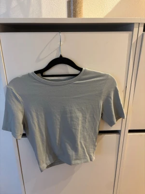 Ljusgrå croppad t-shirt - En enkel och stilren ljusgrå croppad t-shirt med rund hals och korta ärmar. Tillverkad i mjuk bomull som känns skön mot huden. Perfekt till jeans eller kjol för en avslappnad look.