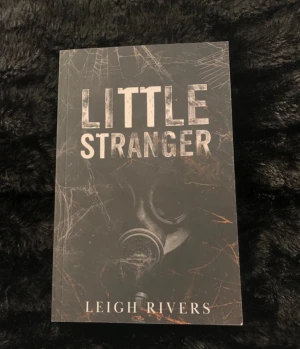 Little Stranger av Leigh Rivers - Säljer boken 'Little Stranger' av Leigh Rivers. Omslaget är svart med ett motiv av en gasmask och spindelnät, vilket ger en mörk och mystisk känsla. Perfekt för dig som gillar spännande och psykologiska romaner. OOP cover!!