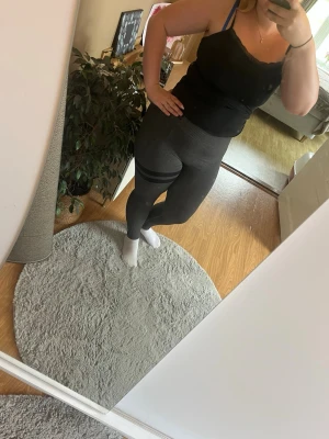 Mörkgrå leggings med svarta ränder - Snygga mörkgrå leggings med två svarta ränder på ena låret. Hög midja och stretchigt material som sitter skönt på kroppen. Perfekta till en tränings look eller när du vill vara bekväm men ändå se stilren ut.