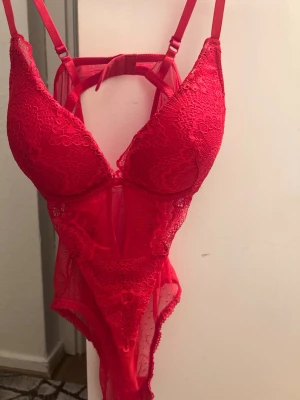 Röd spetsbody från H&M - Snygg röd body från H&M i spets med vadderade kupor och justerbara axelband. Bodyn har fina spetsdetaljer, meshpartier och en djup urringning framtill. Perfekt för dig som vill ha något extra till underklädesgarderoben.