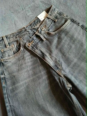 Grå jeans med crisscross midja från Zara - Ett par supersnygga jeans med omlott midjedesign som stängs med knappar. Jeansen är populära och helt slutsålda 🩶