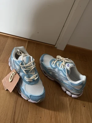 Asics gel-nyc babyblue/white  - Asics sneakers i vitt och ljusblått med mesh och mockadetaljer. Skorna har vita snören och en chunky sula i vitt. Sidan pryds av ett mönster och GEL-detalj baktill. Perfekta för dig som gillar sportig och trendig stil.
