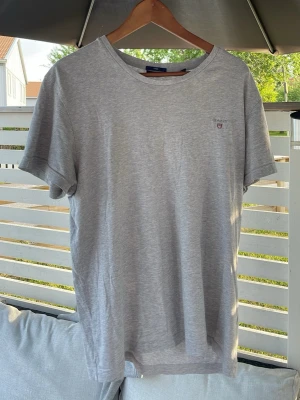 Ljusgrå basic t-shirt med liten GANT logga - En stilren ljusgrå t-shirt i bomull med rund hals och korta ärmar. T-shirten har en liten diskret logga på bröstet och passar perfekt till jeans eller shorts. Enkel och clean design som funkar till det mesta.