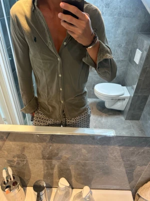 Olivgrön skjorta från Ralph Lauren  - Säljer en olivgrön skjorta från Ralph Lauren som har en snygg urtvättad nyans. Skjortan är i riktigt bra skick. Jag är 188cm och bör storlek S på bilden vilket funkar men inte helt optimalt. Hör av er vid fler frågor:)