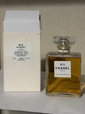 Chanel No 5 Eau de Parfum 100 ml - Chanel No 5 Eau de Parfum i en elegant, rektangulär glasflaska med genomskinlig, facetterad kork. Parfymen har en klassisk guldfärgad vätska och kommer med originalkartong. En ikonisk doft från Chanel, tillverkad i Frankrike.