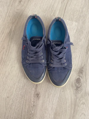 Blå låga sneakers Tommy Hilfiger - Snygga blå sneakers från Tommy Hilfiger med lågt skaft och vita sulor. Skorna har textilöverdel, klassisk snörning och små Hilfiger-detaljer på sidan. Perfekta för en avslappnad och trendig stil.