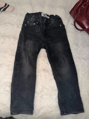 Svarta raka jeans - Snygga svarta jeans med raka ben. Jeansen har en lätt tvättad look och normal midja. Perfekta till vardagsstilen och passar till det mesta. Materialet är denim och de har bälteshällor samt knapp- och dragkedjegylf. Passar barn som är 5 år. 