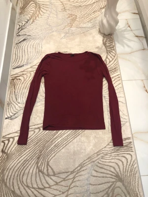Vinröd långärmad topp Gina Tricot - En enkel och stilren vinröd långärmad topp från Gina Tricot. Toppen har en rund halsringning och är gjord i ett mjukt material som sitter snyggt mot kroppen. Perfekt att matcha med jeans eller kjol för en clean look. Är öppen för prisförslag😊
