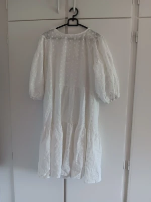 Vit broderad långklänning - Luftig vit klänning med broderade detaljer och volang. Klänningen har trekvartsärm och är tillverkad i ett lätt bomullstyg med hålbroderi. Perfekt för varma dagar och ger en romantisk känsla. Varan är oanvänd 