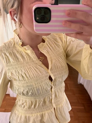 Gul smockad blus med volanger - Söt ljusgul blus med smockdetaljer över bröstet och midjan samt volangkant nedtill. Från Nelly och är endast testad🥰