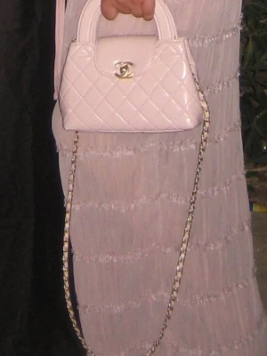 Ljusrosa handväska - Supersöt ljusrosa handväska. Väskan har ett kort handtag och en lång kedjerem i guld och rosa, perfekt för att bära crossbody eller i handen. Liten och smidig modell med elegant look.
