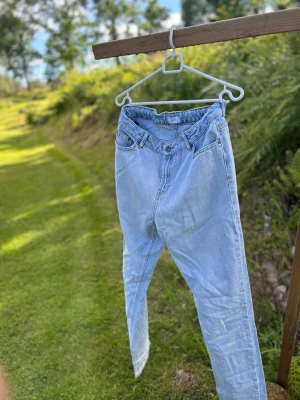 Ljusblå jeans från Grunt - Ljusblå jeans från Grunt med hög midja och avslappnad passform. Klassisk femficksmodell med knappgylf och resår i midjan baktill. Tillverkade i mjukt denimtyg som ger en skön vintagekänsla.