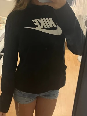 Svart Nike hoodie med stor logga - Säljer en svart hoodie från Nike med stor vit logga och swoosh på bröstet. Hoodien har huva och långa ärmar. Tillverkad i mjukt material som känns skönt mot huden. 